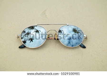 Mirrored sunglasses close up on the beach sand with palm trees reflection.