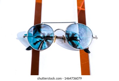 Mirrored Sunglasses On White Wooden Beach Chair With Palm Trees Reflection