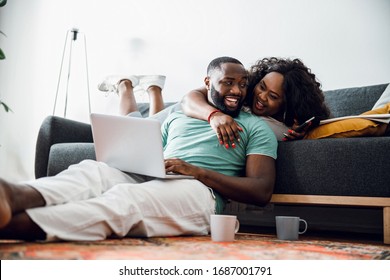 Mirthful lady lying on the sofa and hugging a man with a laptop sitting near - Powered by Shutterstock