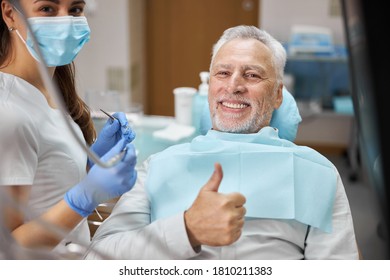 Mirthful Senior Citizen Smiling And Showing Thumbs Up At Dental Appointment With His Dentist And Looking At The Camera