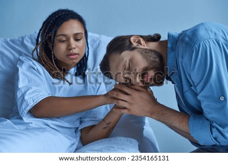 miscarriage concept, sad man grieving and holding hands of african american wife, hospital ward