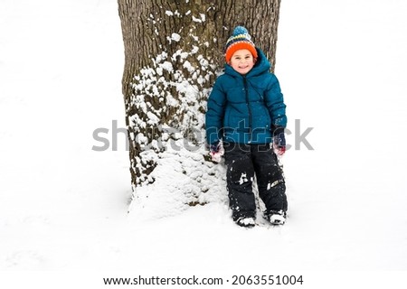 Mischievous boy hiding behind a tree in the snow
