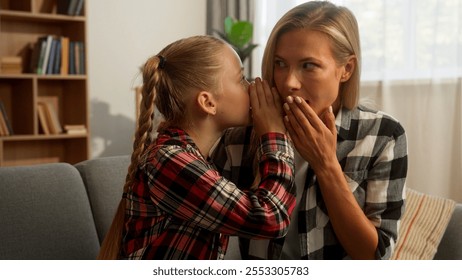 Mischievous Caucasian girl child whispering secret in ear female mother mom shocked surprised woman listen little daughter gossip telling interesting story rumor kid speak with parent at home family - Powered by Shutterstock