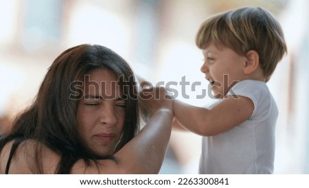 Mischievous child hurting mother. Parenting concept of mom being hit in the head by 2 year old toddler boy. Terrible two concept. Childhood stress concept