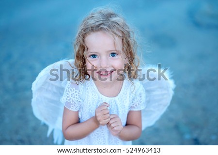 Mischievous little angel girl standing with your clenched fists. It looks like keep  fingers crossed for you.