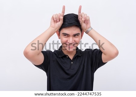 A mischievous man makes horns with two fingers like an imp. Isolated on a white backdrop.