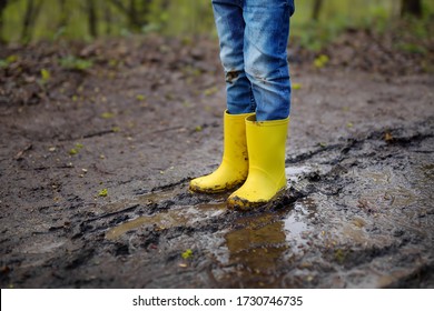 Mischievous preschooler child wearing yellow rain boots walking by muddy road. Kid playing and having fun. Outdoors games for children.
