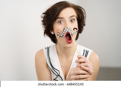 Mischievous Young Woman With A Party Accessory Polka Dot Mustache Held To Her Lips As She Pulls A Quirky Face For The Camera