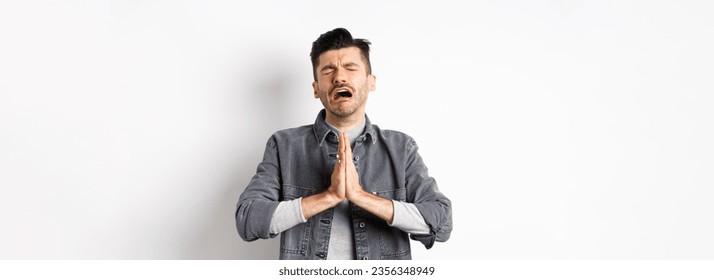 Miserable man begging for help, need something and crying, pleading with sad face, standing on white background desperate.