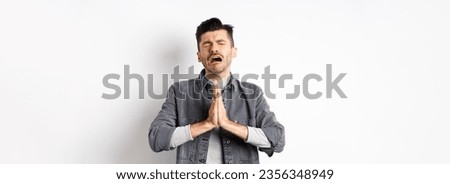 Miserable man begging for help, need something and crying, pleading with sad face, standing on white background desperate.