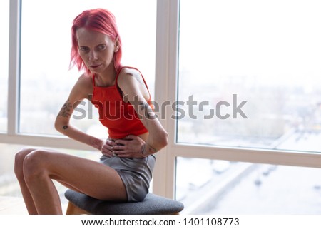 Miserable woman. Unhealthy miserable woman with anorexia sitting near the window feeling awful Imagine de stoc © 