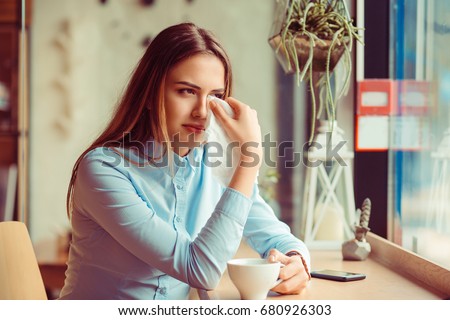 Misery, infelicity. Brunette woman girl about to cry wiping tears sneezing in a tissue drinking tea, coffee, hot beverage. Negative human emotion, face expression, reaction, body language