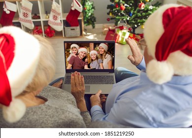 Missing Children And Grandchildren On Christmas Holidays In Lockdown. Back View Of Happy Grandparents In Santa Caps Sitting On Couch Together, Video Calling Their Family And Waving Hands At Screen