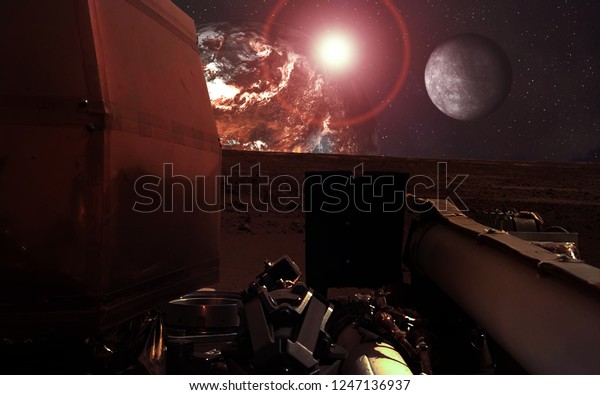 Mission InSight Mars Lander in shadow  near the red\
 planet and moon with lens flare. Elements of this image were\
furnished by NASA.