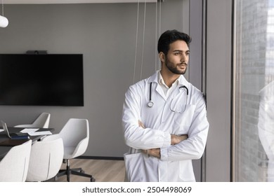 Mission, medical worker career. Serious male doctor in white coat take break, gazing out window standing in conference room after medical council, look in city view, full of aspirations and daydreams - Powered by Shutterstock