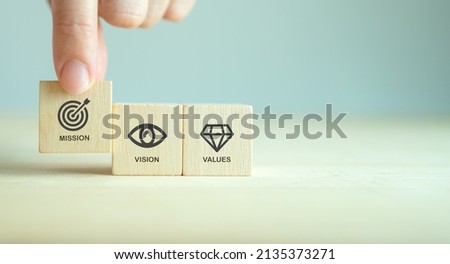 Mission, vision and values of company. Purpose business concept. Hand holds wooden cube with mission symbol and vision, values symbols on grey background. Modern flat design. Business presentation.