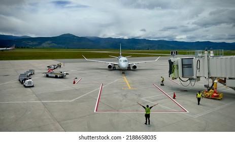 MISSOULA MONTANA AIRPORT, MT, JUN 2022: Wide View American Airlines Embraer E175 Jet Aircraft Approaches Gate With Ground Crew And Vehicles Around It, Mountains In Background