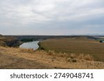 The Missouri River winds between open fields near Fort Benton, Montana, with distant mountains and a cloudy sky softening the landscape.