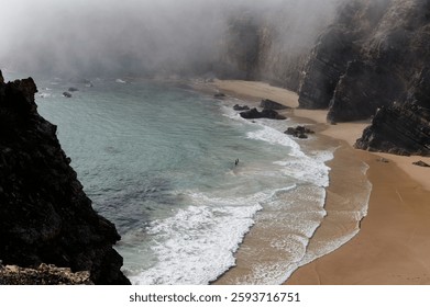 Mist drapes over the rugged cliffs of Praia do Tonel as gentle waves kiss the secluded shore.