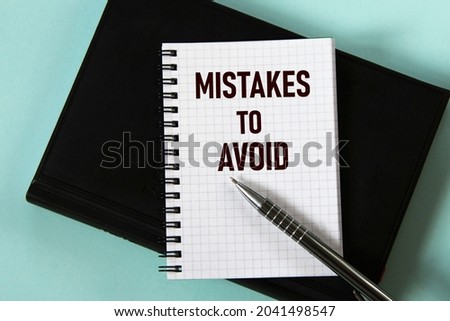 MISTAKES TO AVOID - words in a white notebook against the background of a black notebook with a pen. Business concept