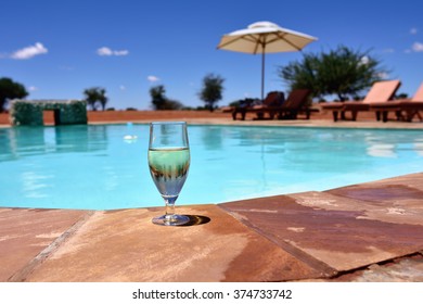 Misted Glass Of White Wine With Ice On The Border Of The Swimming Pool In The Middle Of Kalahari Desert. Concept Exotic Luxury Vacation. Small Depth Of Field