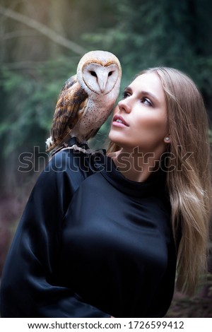 Misterioius young blond girl with a barn owl white bird in a foggy forest in a blue dress