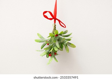 Mistletoe branch with red ribbon hanging against light wall - Powered by Shutterstock