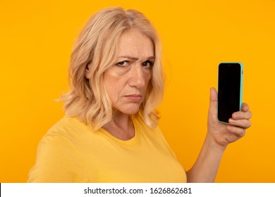 Mistrust angry woman with phone using it isolated in the yellow studio.