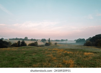 A misty countryside morning overlooking multiple agricultural farmland fields. Morning dew on the tree lined grass. British outdoors in the morning with low cloud and blue  pink sky - Powered by Shutterstock