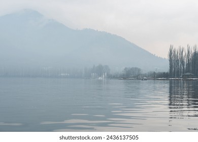 Misty Dal lake in Srinagar on the afternoon of January in Jammu and Kashmir. Still water with bare trees and shikaras in the background. - Powered by Shutterstock