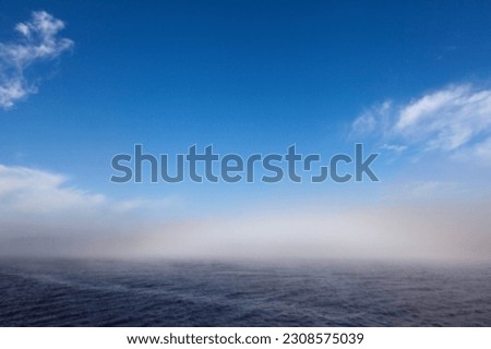 Misty, foggy weather at sea. Sea smoke above the water. Blue sky, daylight, and summer.