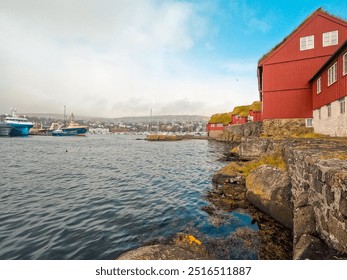 Misty Harbor Views in Tórshavn, the Capital city of the Faroe Islands. Red Scandinavian style buildings with grass rooftops on the rocky shoreline of the North Atlantic Ocean. Large ships moored. - Powered by Shutterstock