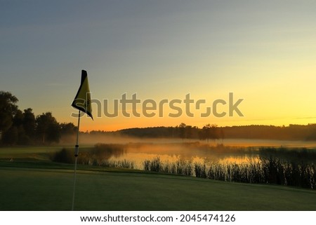 Misty landscape in the early morning at a golf course. Single golf flag. Sun rising in the east. Next to a small lake. Vallentuna, Stockholm, Sweden, Scandinavia, Europe.
