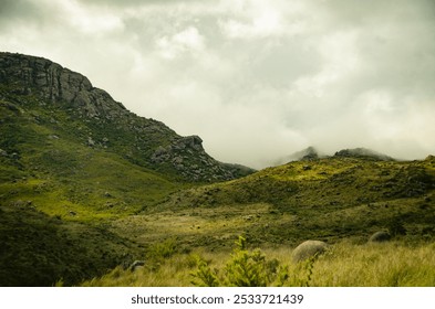 A misty landscape in Itatiaia National Park featuring rolling green hills and rocky formations under a cloudy sky. - Powered by Shutterstock