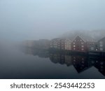 Misty morning in Trondheim, Norway, with traditional colorful wooden buildings along the Nidelva River shrouded in thick fog