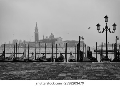 Misty morning in Venice with gondolas lined along the dock, showcasing the silhouette of historic buildings - Powered by Shutterstock