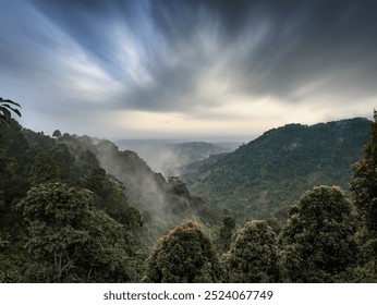 A misty mountain landscape with dense forest and dramatic sky, creating a calm and serene atmosphere during the early morning - Powered by Shutterstock