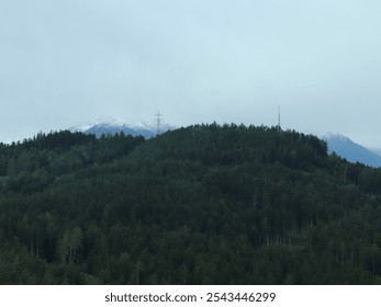 Misty Mountain Landscape with Dense Forest, Snow-Capped Peaks, and Telecommunication Towers in Innsbruck, Austria - Powered by Shutterstock