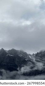 Misty mountain landscape with dramatic clouds covering rocky slopes and creating a mysterious atmosphere.
