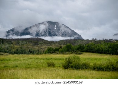 Misty mountain landscape with green fields and patches of trees under a cloudy sky - Powered by Shutterstock