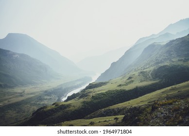 Misty mountain landscape with hills and rocks on background of wide mountain river in mist. Atmospheric scenery with mountain relief and big river in dark green valley in rainy weather. Gloomy weather