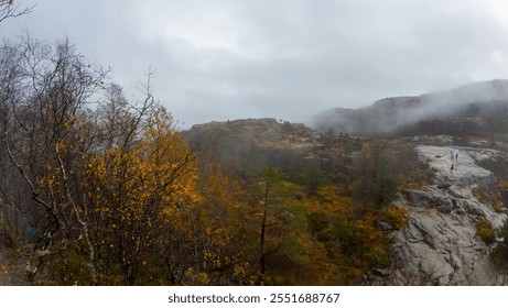 A misty mountain landscape with rocky terrain and autumn foliage. The scene features trees with yellow leaves, rocky outcrops, and a cloudy sky, creating a serene and atmospheric environment. - Powered by Shutterstock