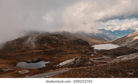 A misty mountain landscape with small lakes, rocky terrain, and a winding road in the distance - Powered by Shutterstock