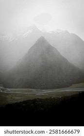 A Misty mountain landscape with a triangular peak shrouded in fog, surrounded by lush greenery and a winding river.
