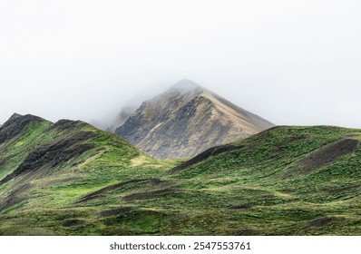 Misty mountain peak surrounded by lush green hills under an overcast sky, showcasing natural beauty and tranquility. - Powered by Shutterstock