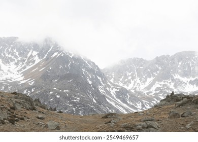 A misty mountain range in Andorra, showcasing snowy peaks and rocky terrain beneath a shroud of clouds. The ethereal atmosphere captures the raw beauty of this alpine landscape.	 - Powered by Shutterstock