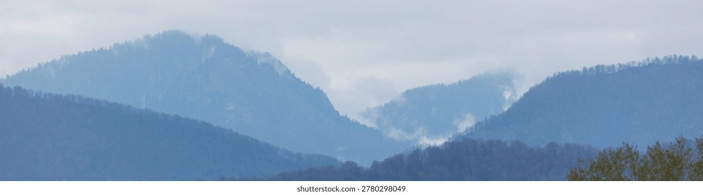 Misty mountain range under cloudy sky. Layers of hills fade into blue haze. No visible animals or plants in frame. Soft natural tones dominate scene. Calm and serene landscape mood