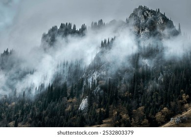 Misty mountain scene with rugged peaks, dark green pine trees, and swirling clouds enveloping the landscape. - Powered by Shutterstock