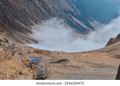 Misty mountain valley shrouded in fog. Dramatic landscape photography showcasing rugged terrain and autumnal colors. Ideal for travel, adventure, and nature themes. Făgăraș Mountains, Romania - Powered by Shutterstock