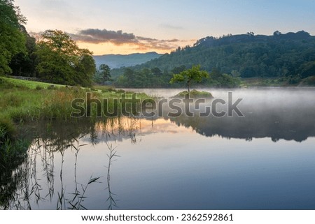 Misty sunrise reflections in lake at Rydal Water, Lake District, UK.